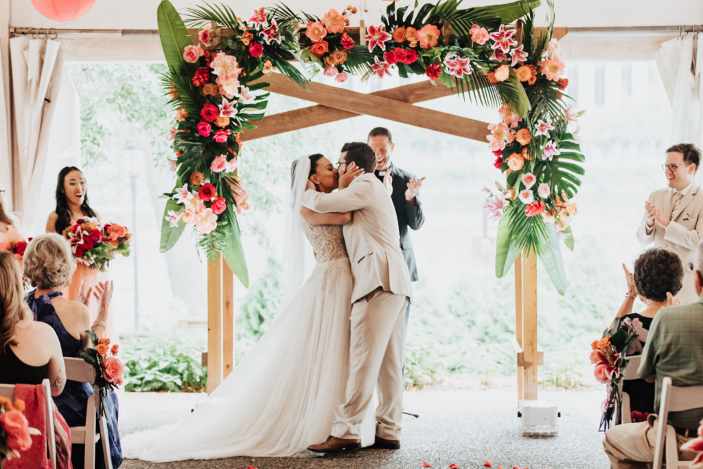 bride and groom ceremony kiss tropical wedding arch arrangement