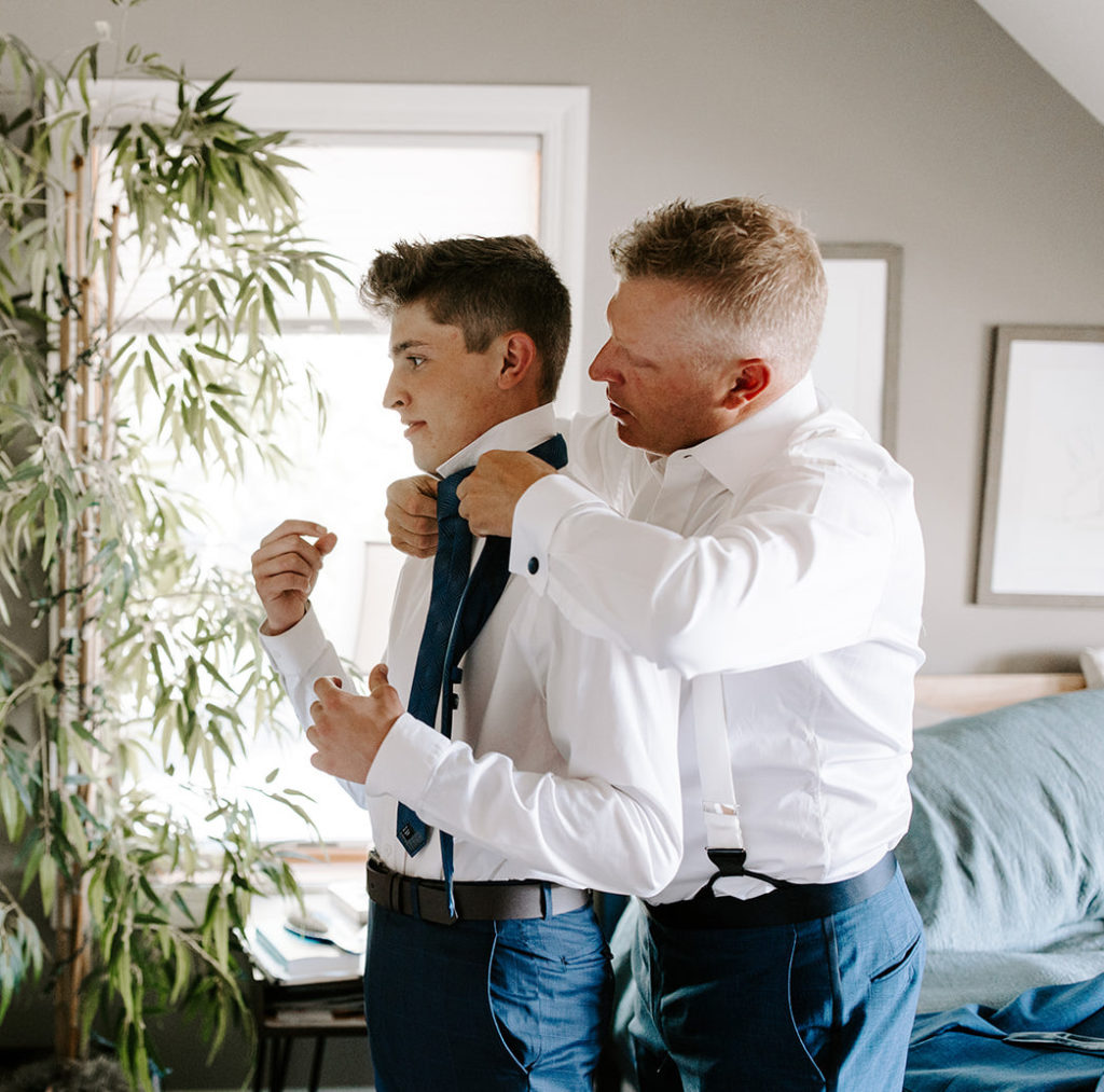 groomsman getting ready tying tie with dad