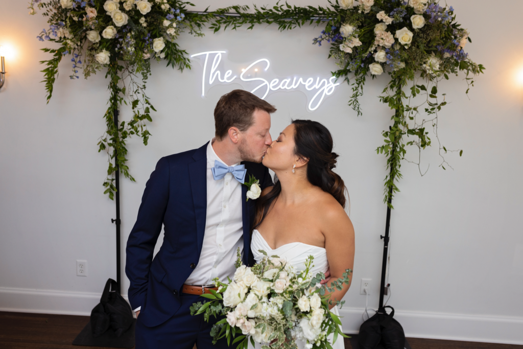 bride and groom kiss in front of last name neon sign