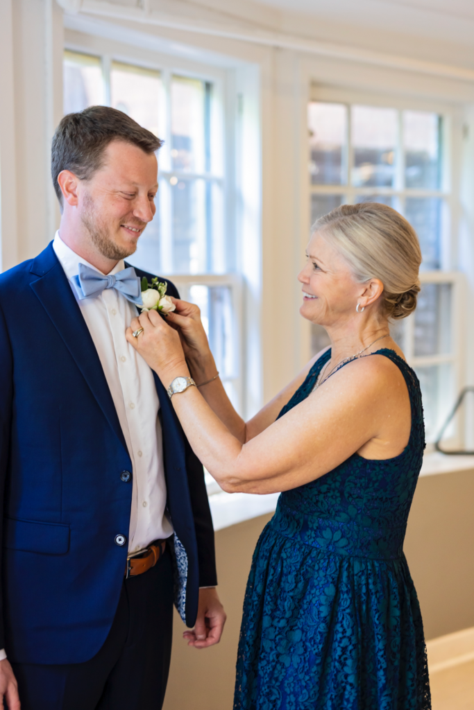 groom getting boutonniere put on by mom