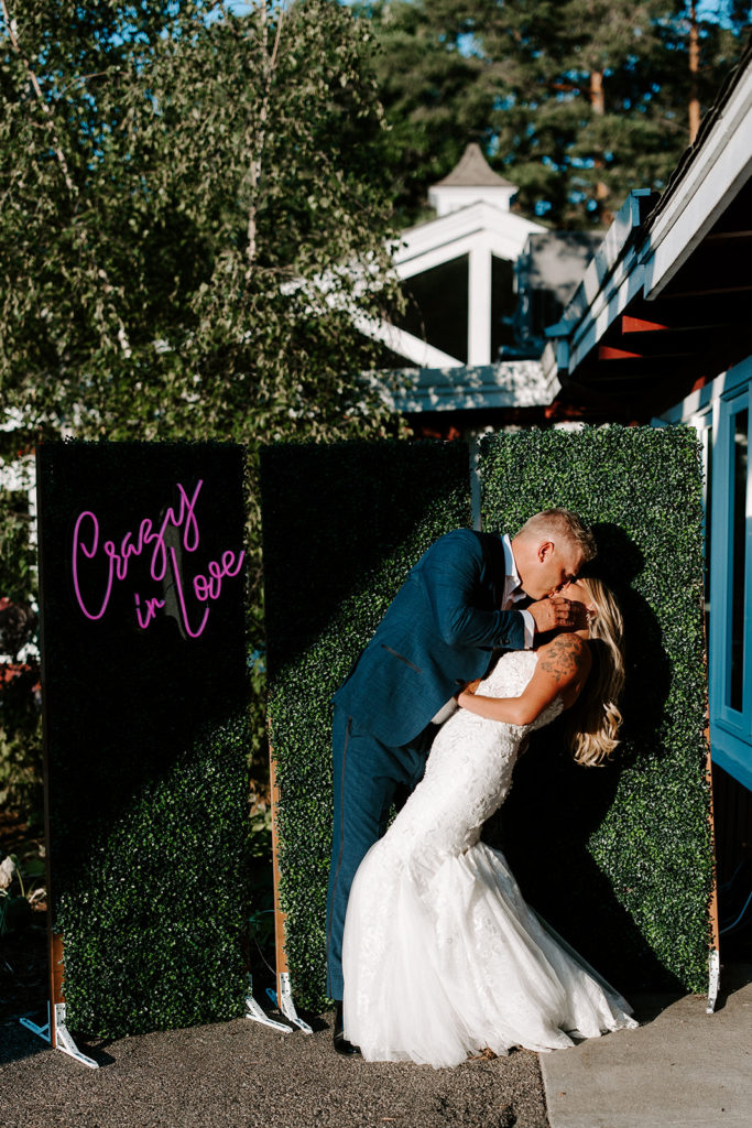 Boxwood backdrop with crazy in love neon sign at Cast & Cru wedding