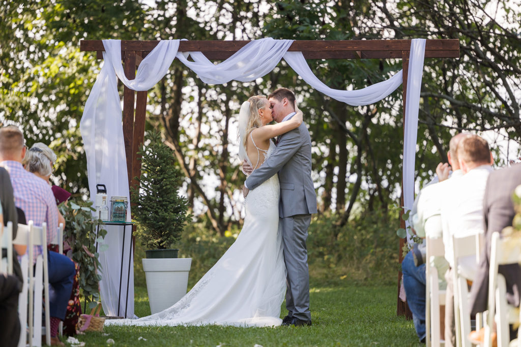 bride-groom-kiss-outdoor-ceremony-wood-arch-draping