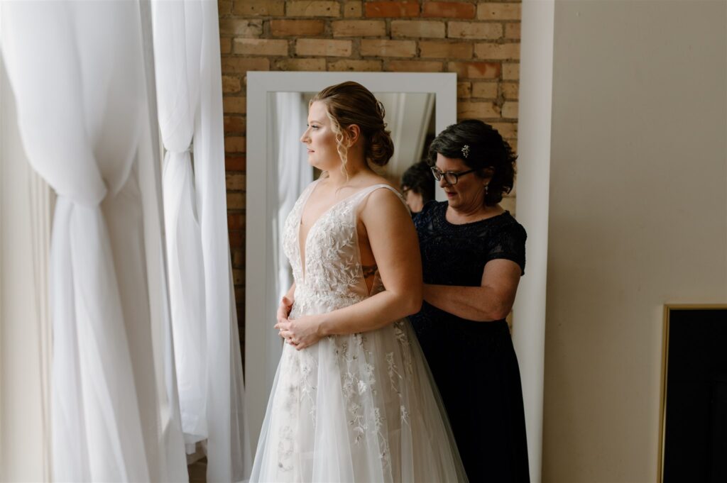 bride putting on wedding dress with mom