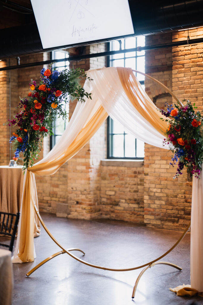 colorful floral and draping on gold circle wedding arch 