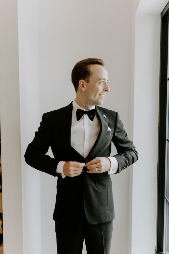 Groom getting ready buttoning black jacket