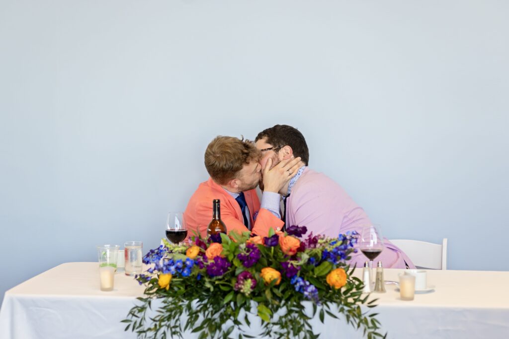 grooms kissing at sweetheart table with colorful florals at walker art center wedding
