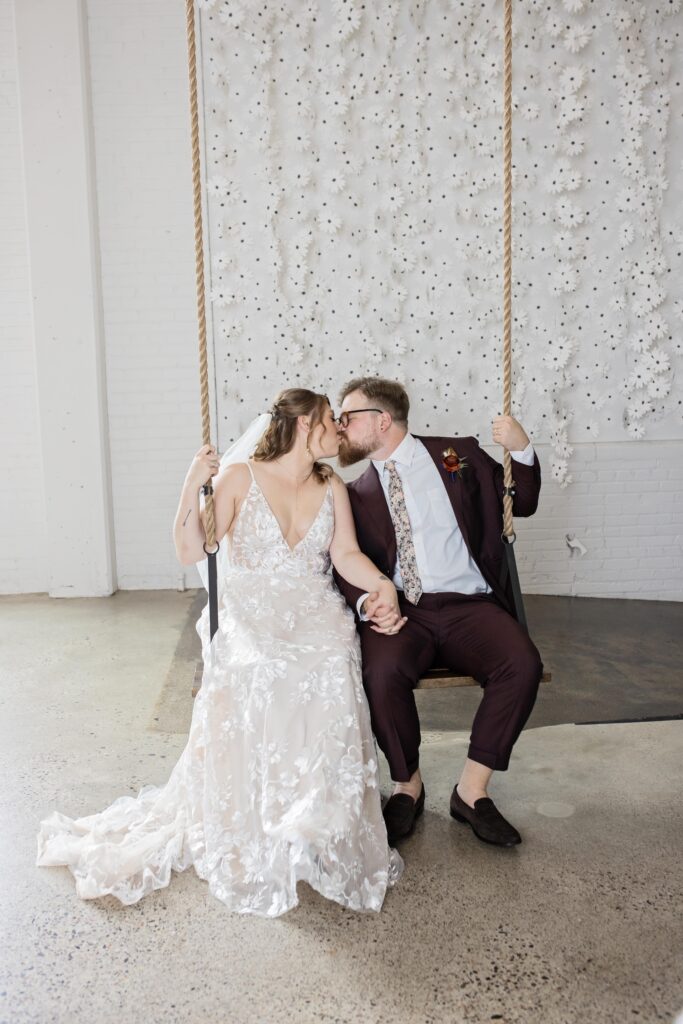 Bride and groom kissing on swing at urban daisy