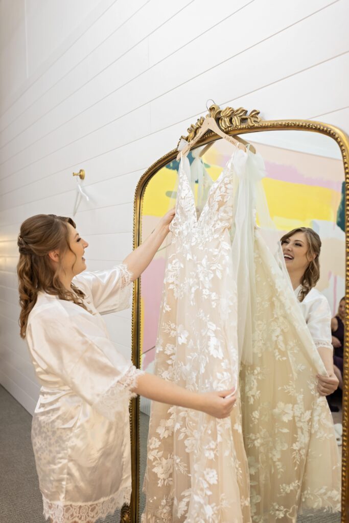 bride looking at wedding dress hanging on mirror at Urban Daisy