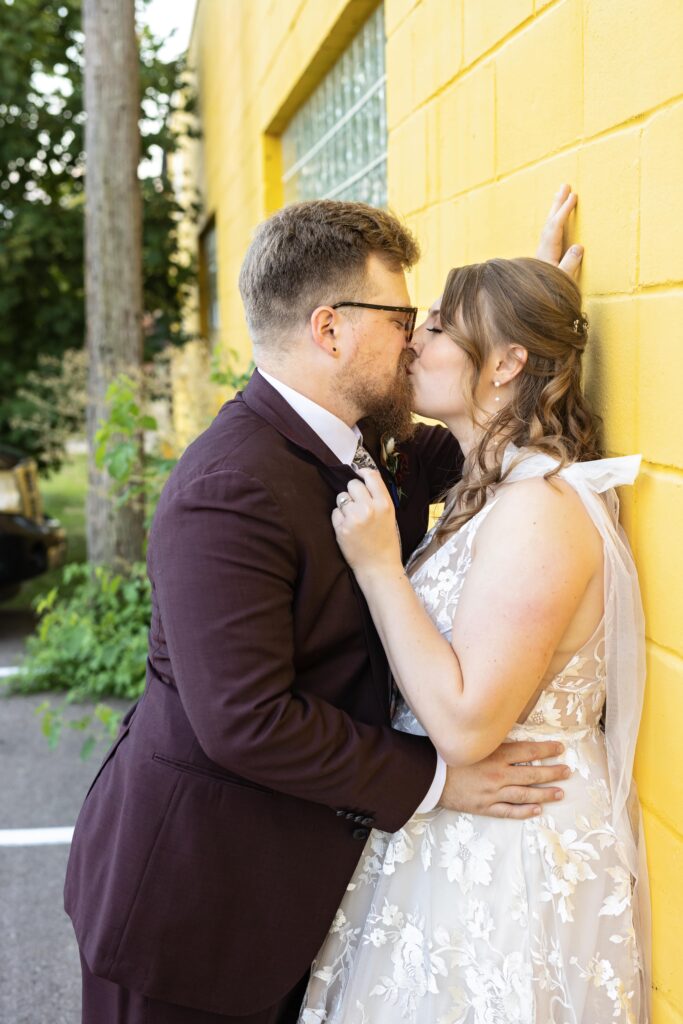 bride and groom kissing against yellow wall in Minneapolis