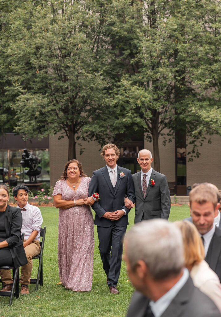 groom walking down the aisle with parents in outdoor ceremony