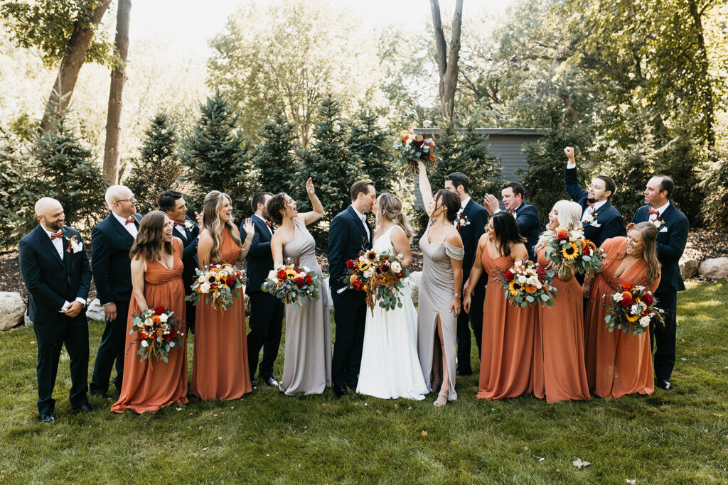 large wedding party cheering for bride and groom kiss