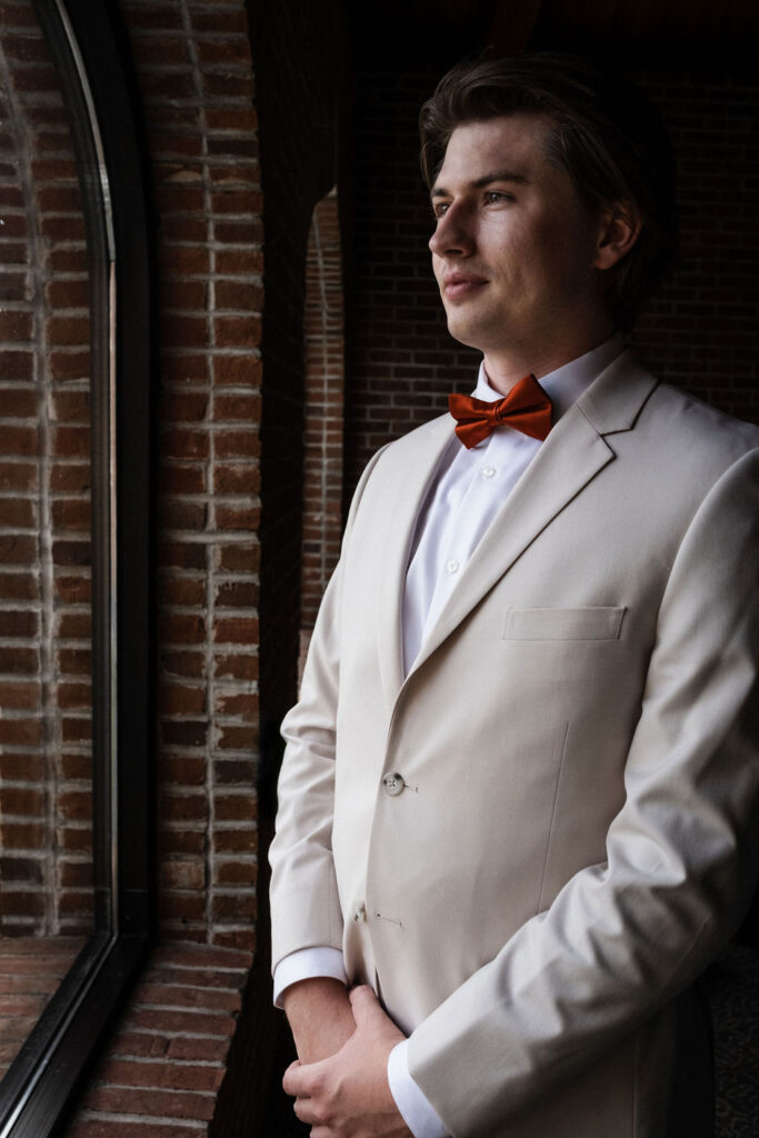 groom getting ready wearing cream suit and red bowtie