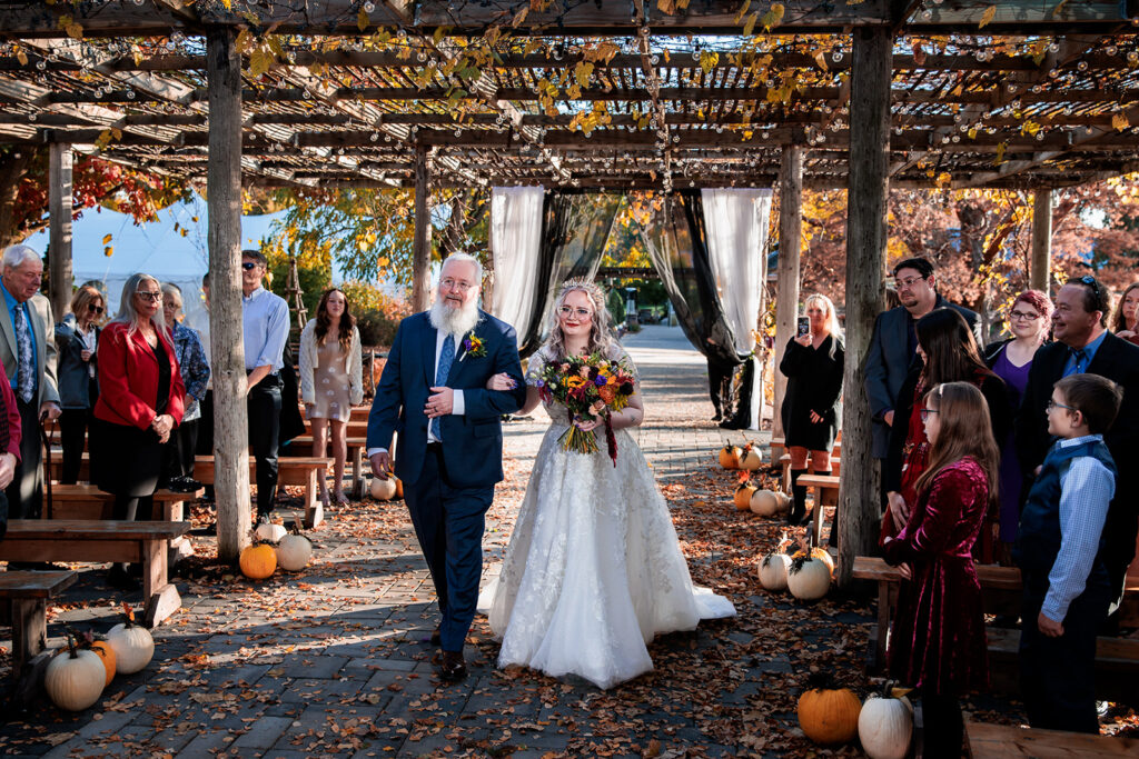 bride escorted down the aisle by her father at outdoor October ceremony