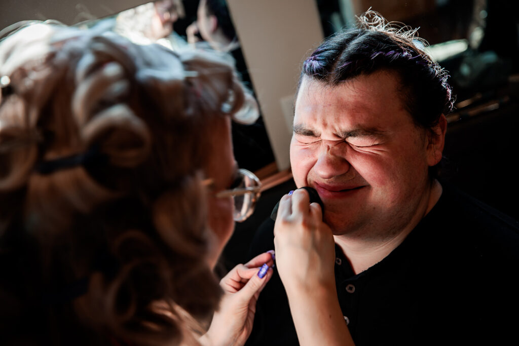 bride helping groom with makeup wedding morning