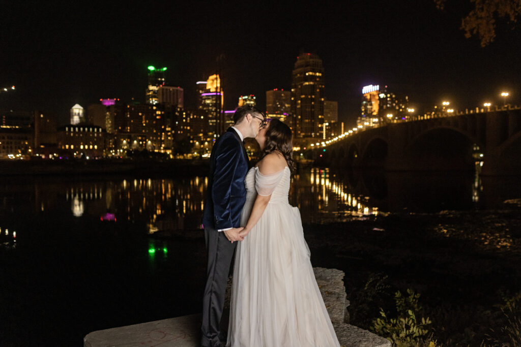 bride and groom kissing in front of Minneapolis skyline at night