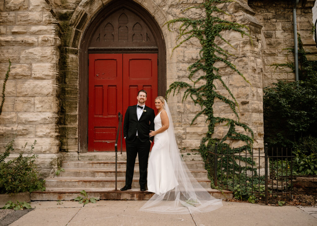 elegant bride and groom portrait in front of red door with cathedral veil