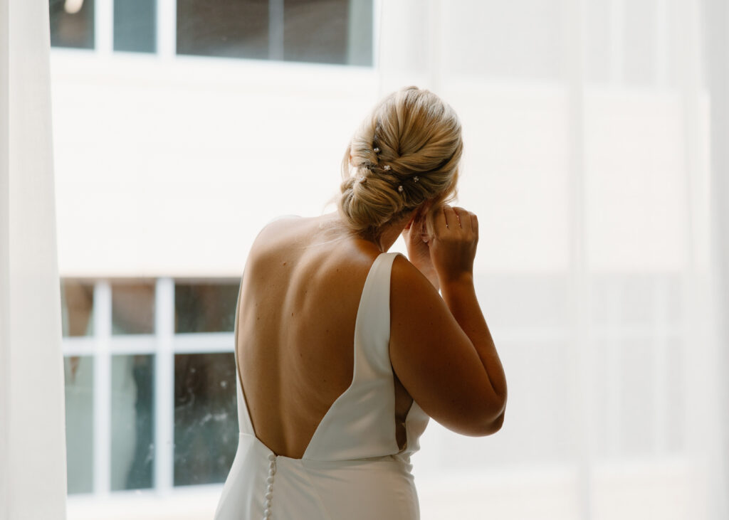 bride putting on earrings with low bridal bun with pearls