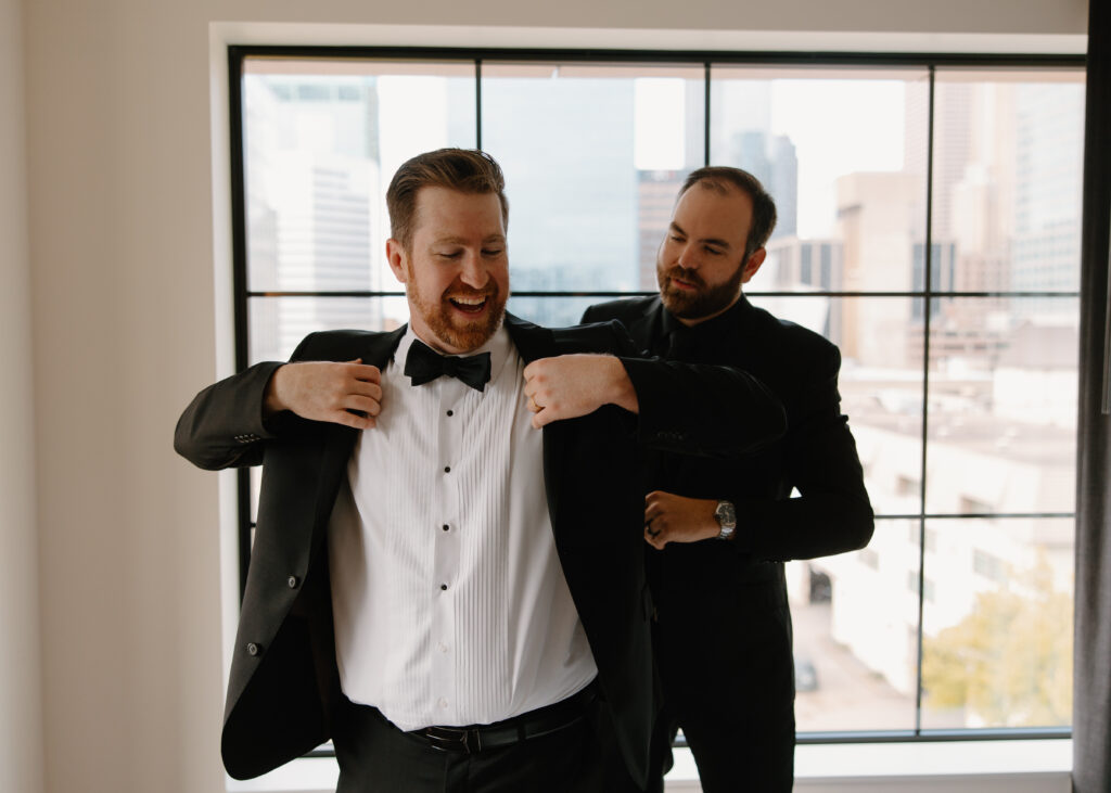 best man helping groom put on suit coat