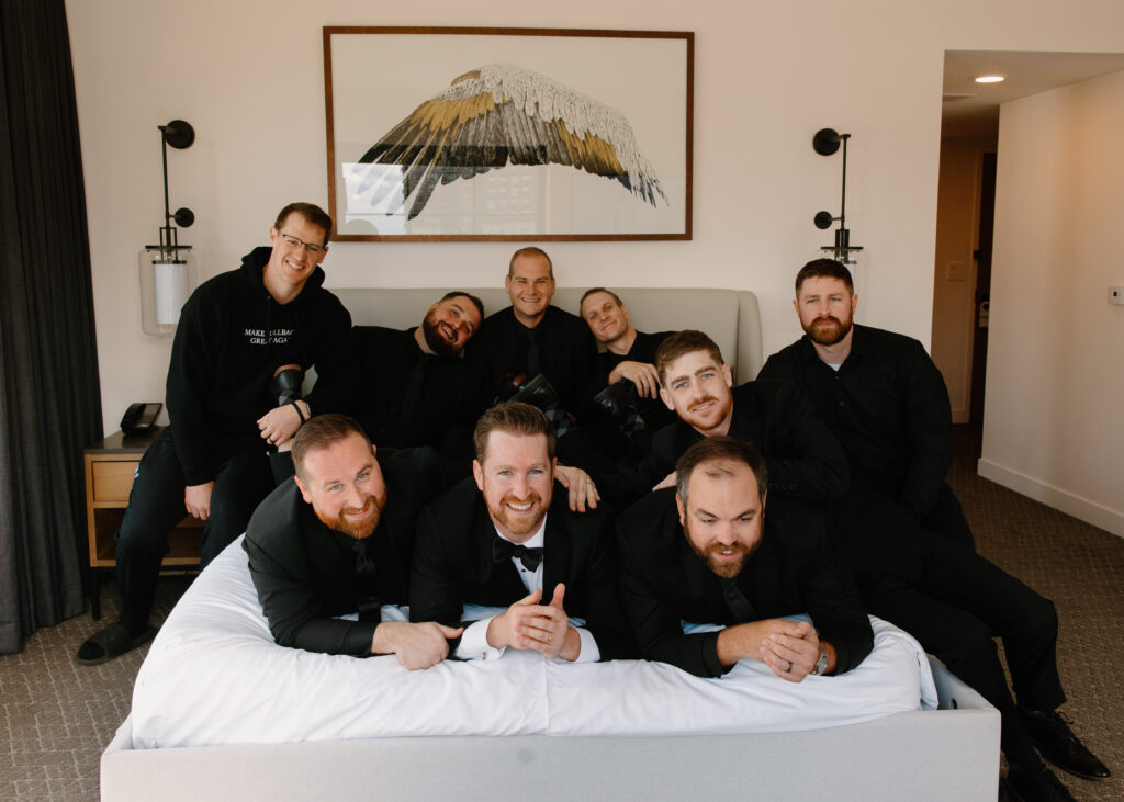 groomsmen posing on hotel bed for getting ready photo