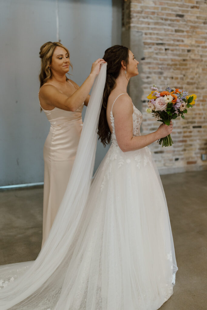 Bridesmaid adjusting bride’s veil before the ceremony.