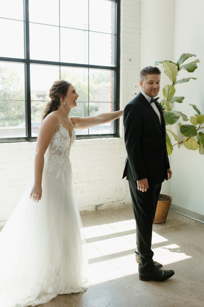 Bride doing a first look with the groom near large windows in a bright indoor space.