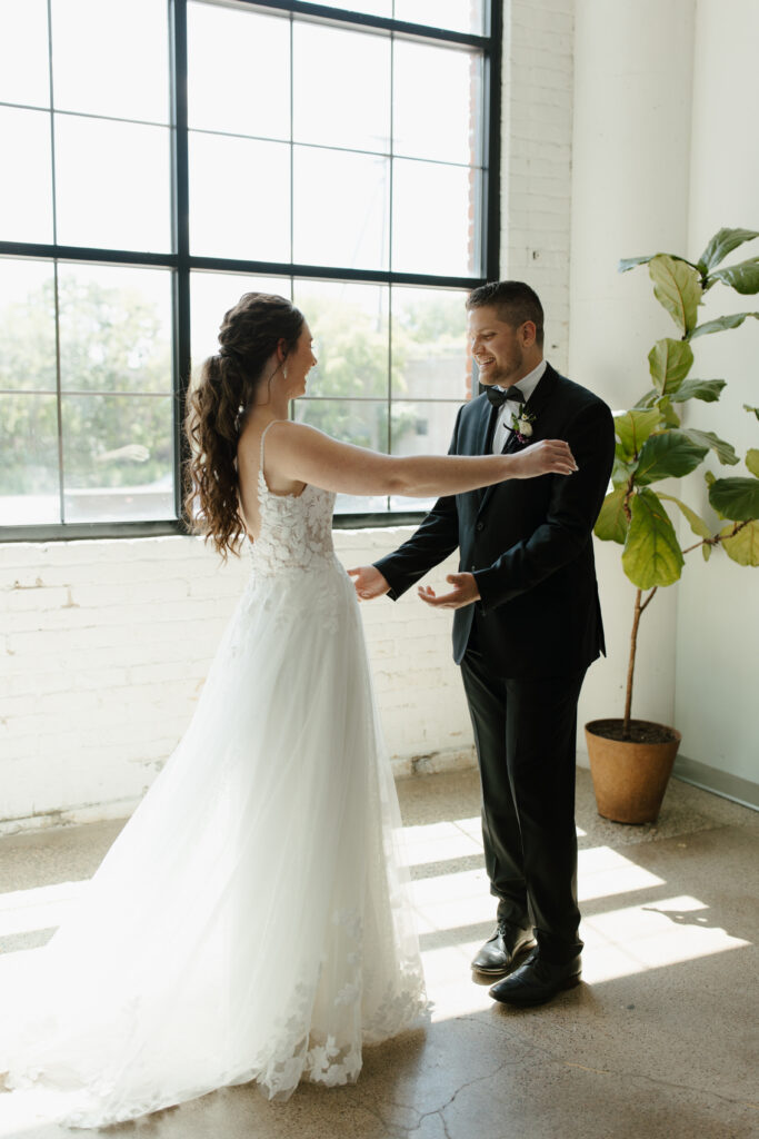 Bride and groom dancing together in a bright room with large windows.