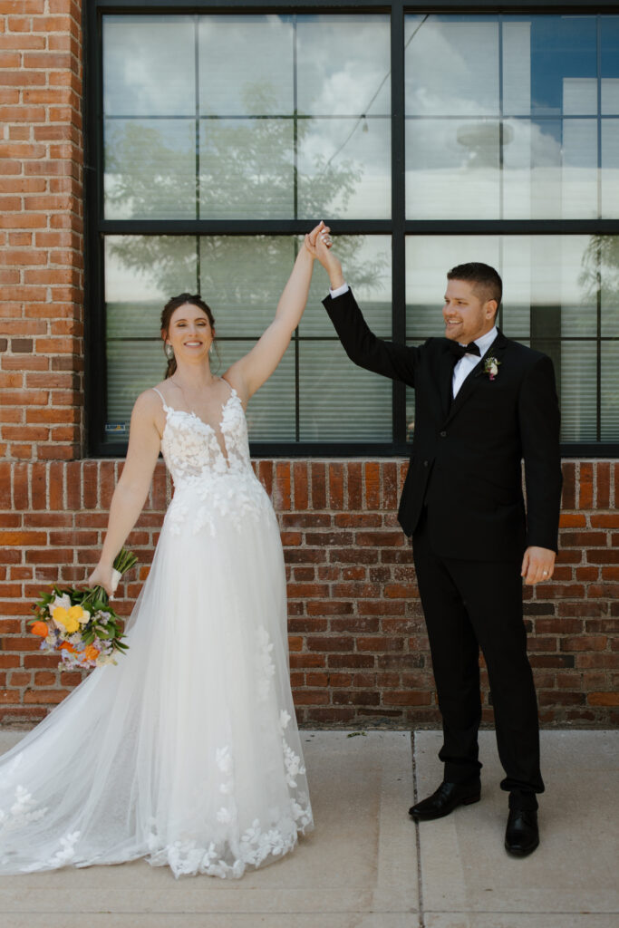 Bride and groom celebrating with a twirl in front of a modern building.