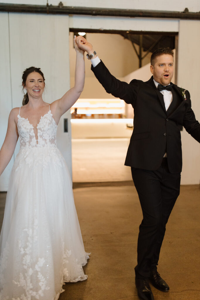 Bride and groom raising their joined hands in celebration inside a wedding venue.