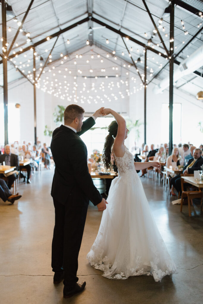 Bride and groom sharing a first dance in a warmly lit reception venue with guests watching.