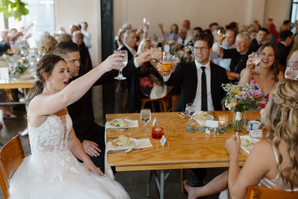 Wedding guests and bridal party raising glasses for a toast at a reception table.