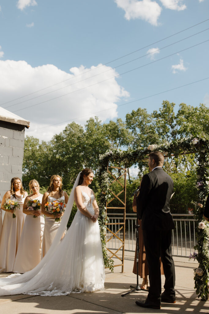 Bride and bridesmaids posing outdoors near trees and a rustic building.