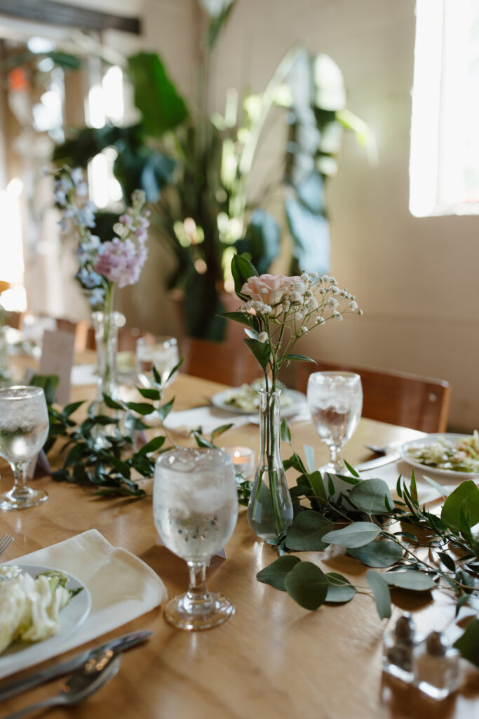 Close-up of wedding table decorations featuring glassware, greenery, and flowers.