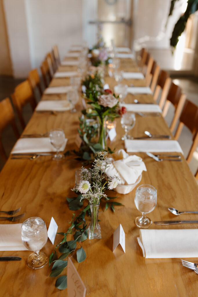 Elegant wedding reception table setup with floral centerpieces and wooden chairs.