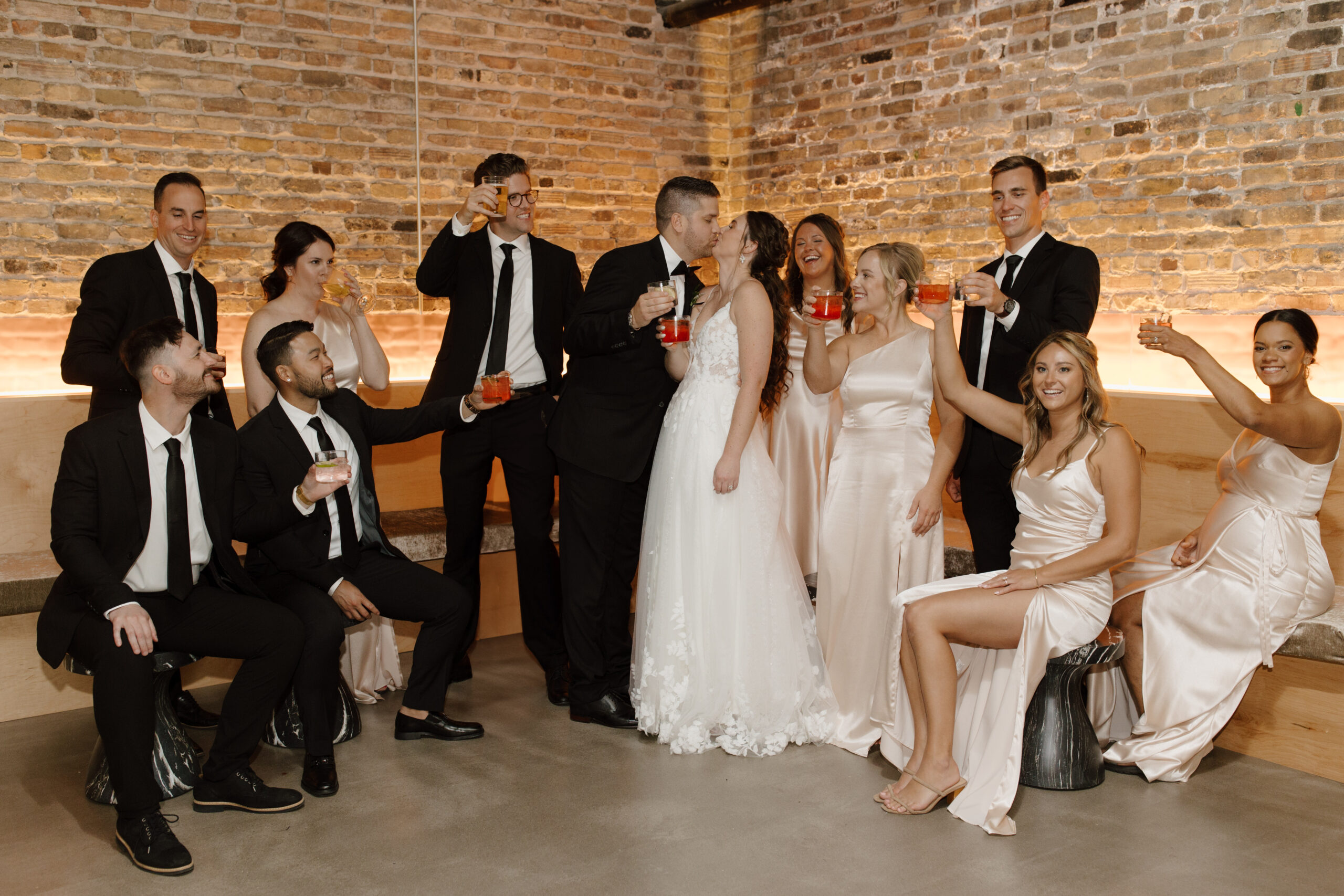 Bridal party cheering and clapping as the bride and groom walk by in an indoor venue with brick walls.
