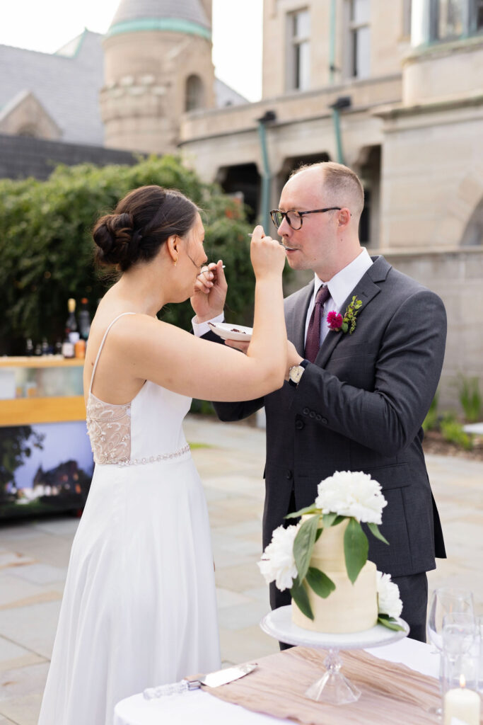 Bride feeds a bite of cake to the groom as they laugh together during the tradition.
