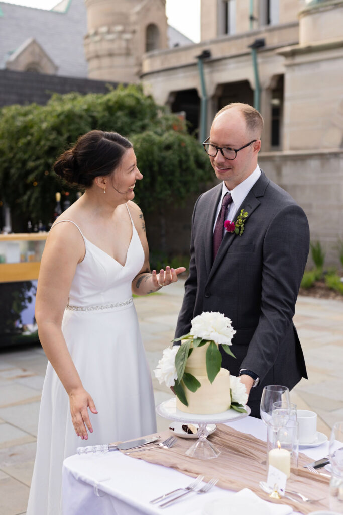 Bride and groom smile as they prepare to cut their simple white wedding cake decorated with a large flower.