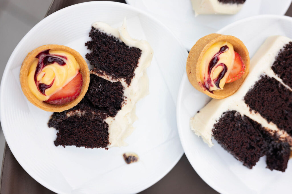 Dessert plate featuring slices of chocolate cake with white frosting and individual fruit tarts topped with plum and berry glaze.