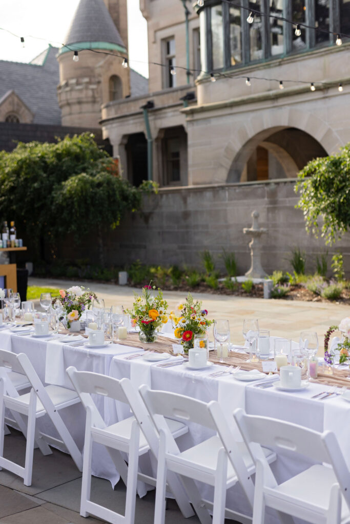 An elegant outdoor reception setup with white chairs and long banquet tables in front of the historic American Swedish Institute.