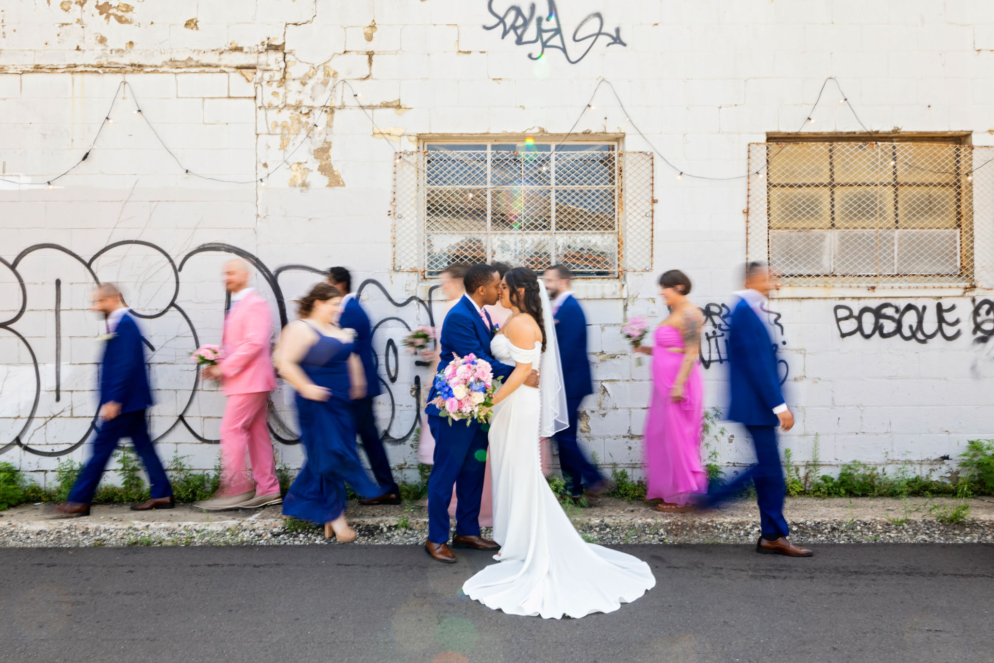 colorful wedding party blurred going around a kissing wedding couple